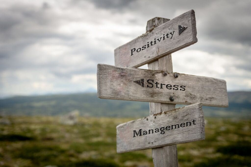 Workplace stress, positivity, and management concepts shown on a wooden road sign, reflecting leadership training and corporate stress management by Ginny Estupinian, PhD